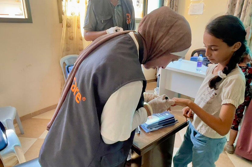 A woman wearing a CARE vest helps a young girl in a health clinic.