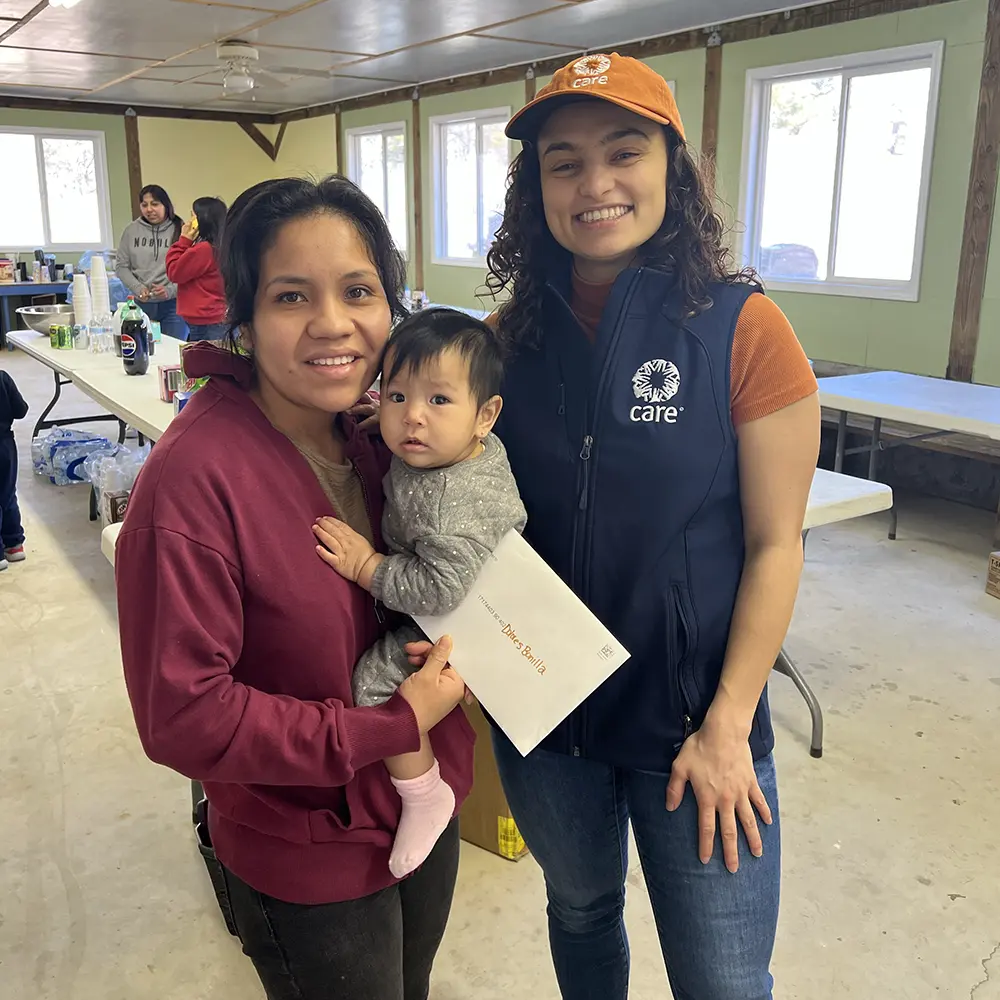 A woman holding a young child and an envelope stands next to a CARE staff member.