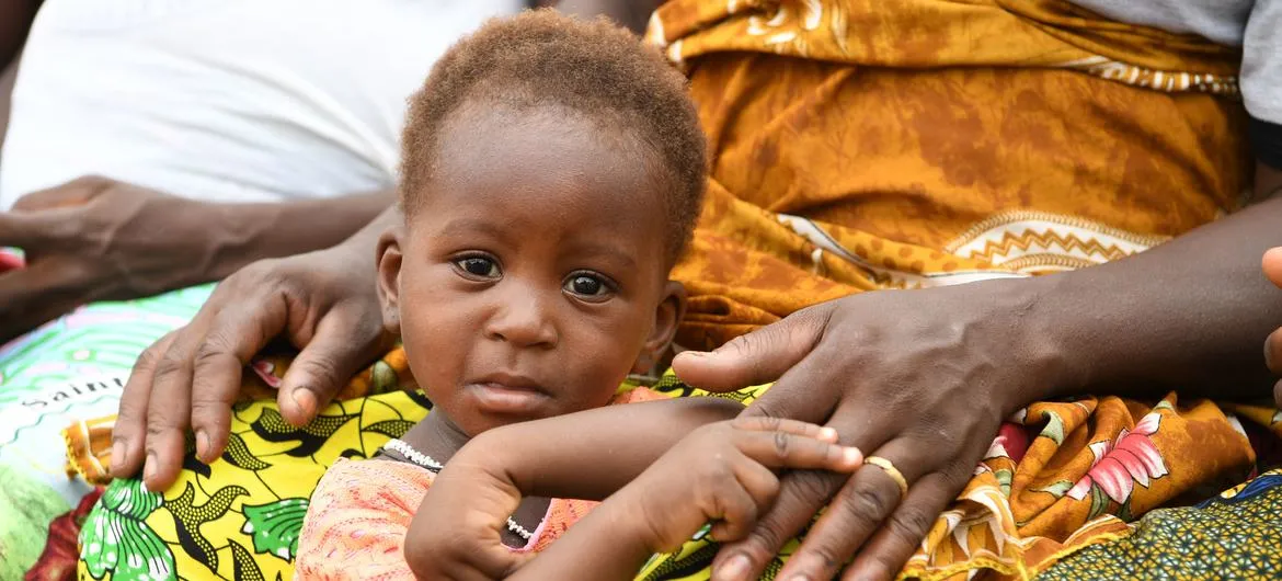 A little girl, holding her mother's hand, gazes at the camera.