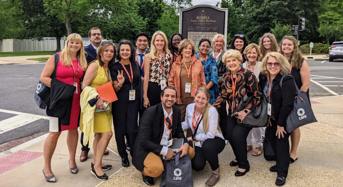 A group of CARE Women’s Network members and friends standing in front of a sign posing for a photo outdoors.