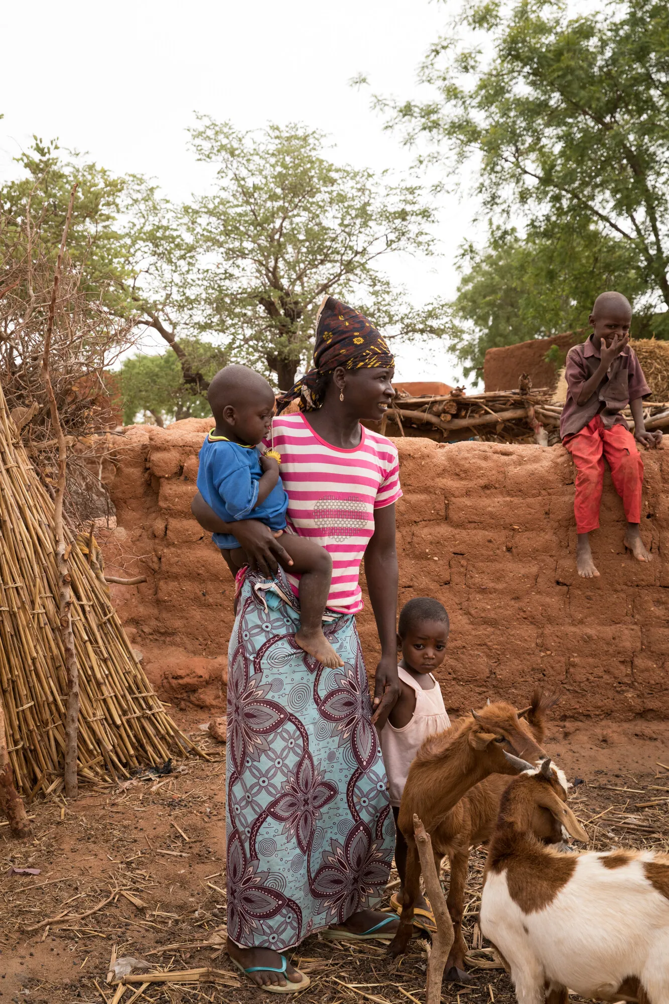 A woman, looking sideways, stands with three young children and two goats.