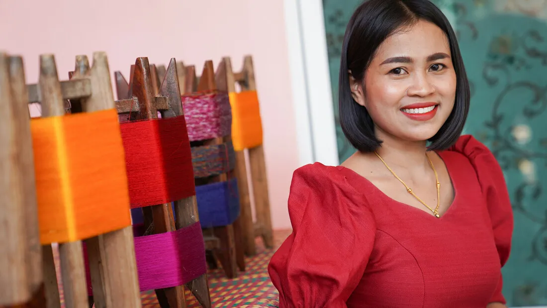 A woman smiling and wearing a red shirt standing next to thread.