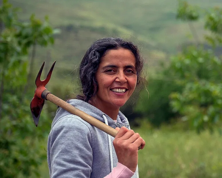 A woman holding a gardening tool and smiling.