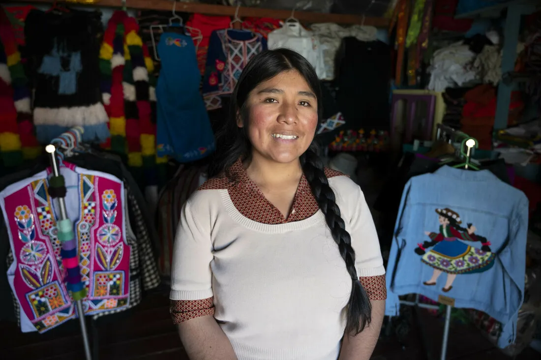 A woman standing and smiling in front of clothes.