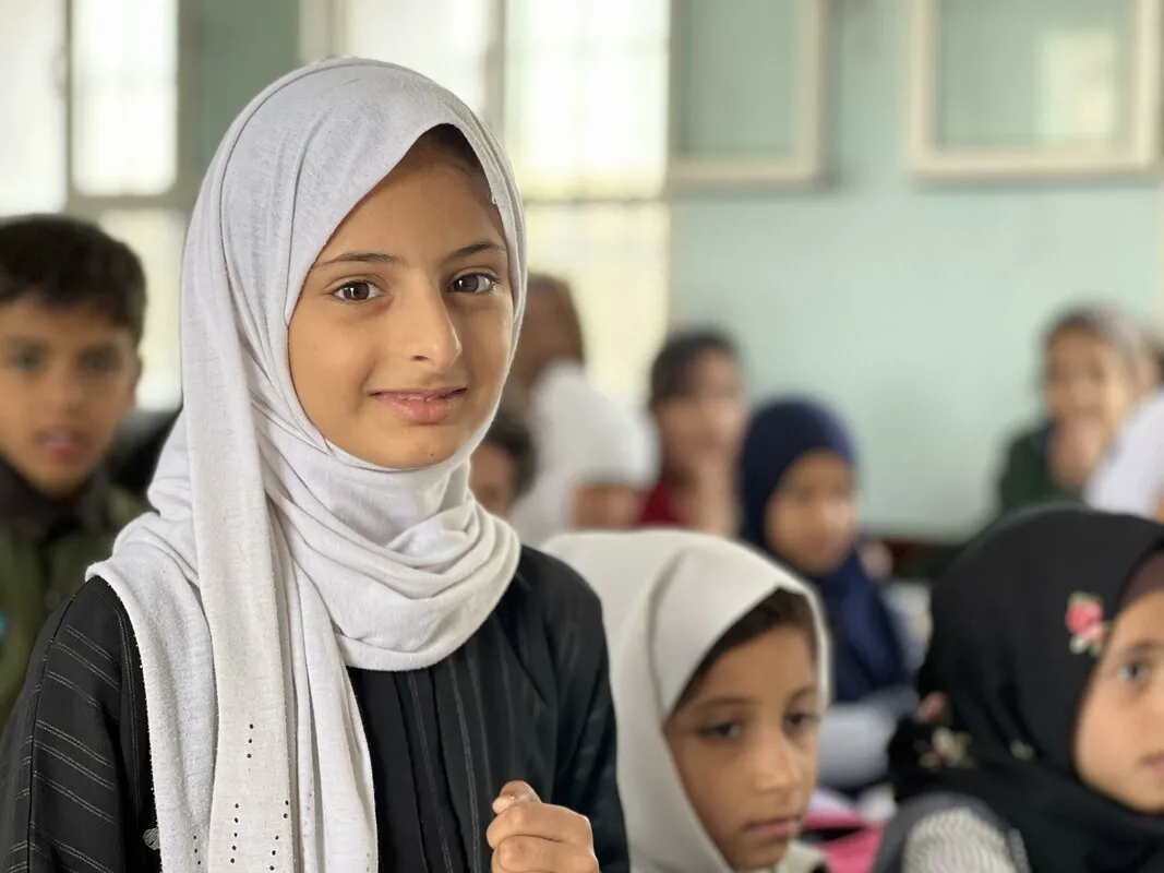 A girl smiling in a classroom with other children.