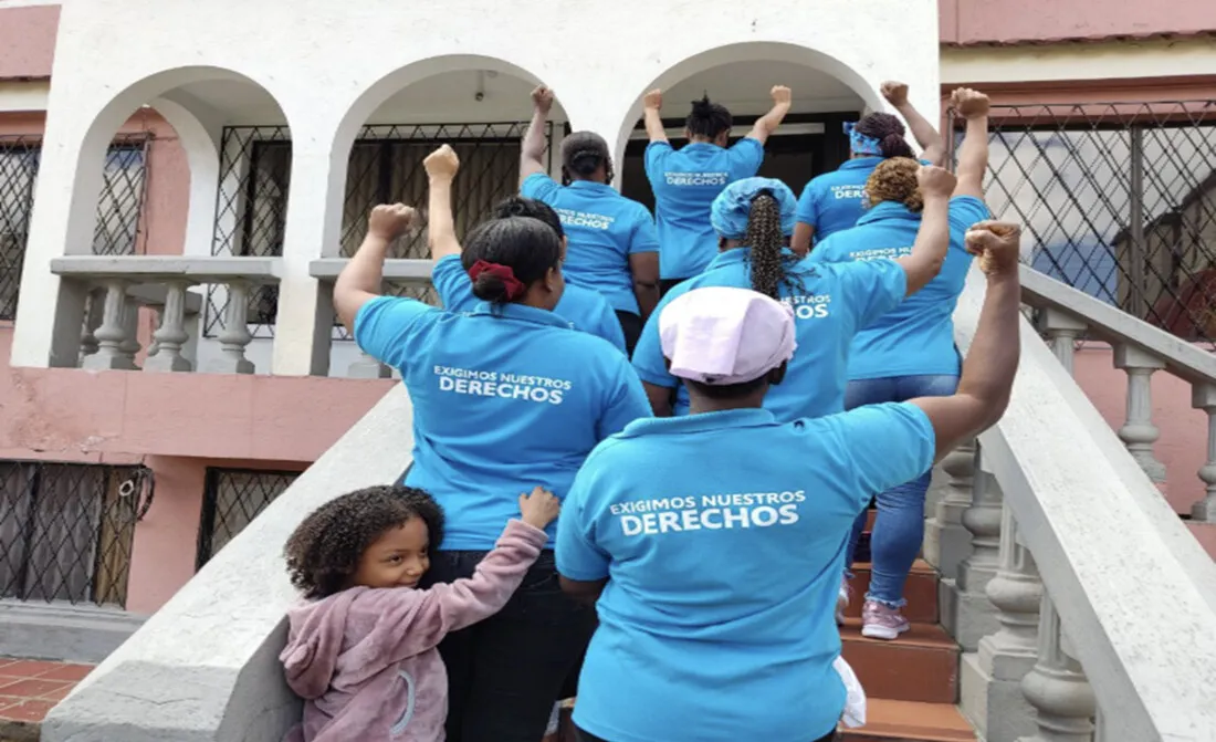 A group of women wearing blue t-shirts raise their hands in solidarity.