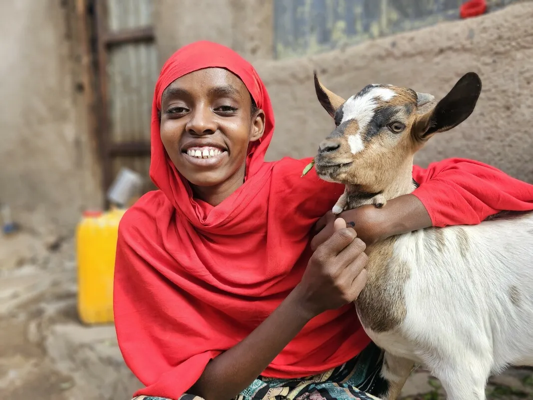A young girl smiling and hugging a goat.