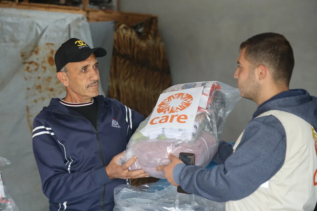 A man hands a bag of CARE-distributed shelter materials to another man.