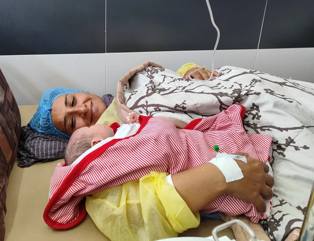 A woman in hospital gown holding infant.