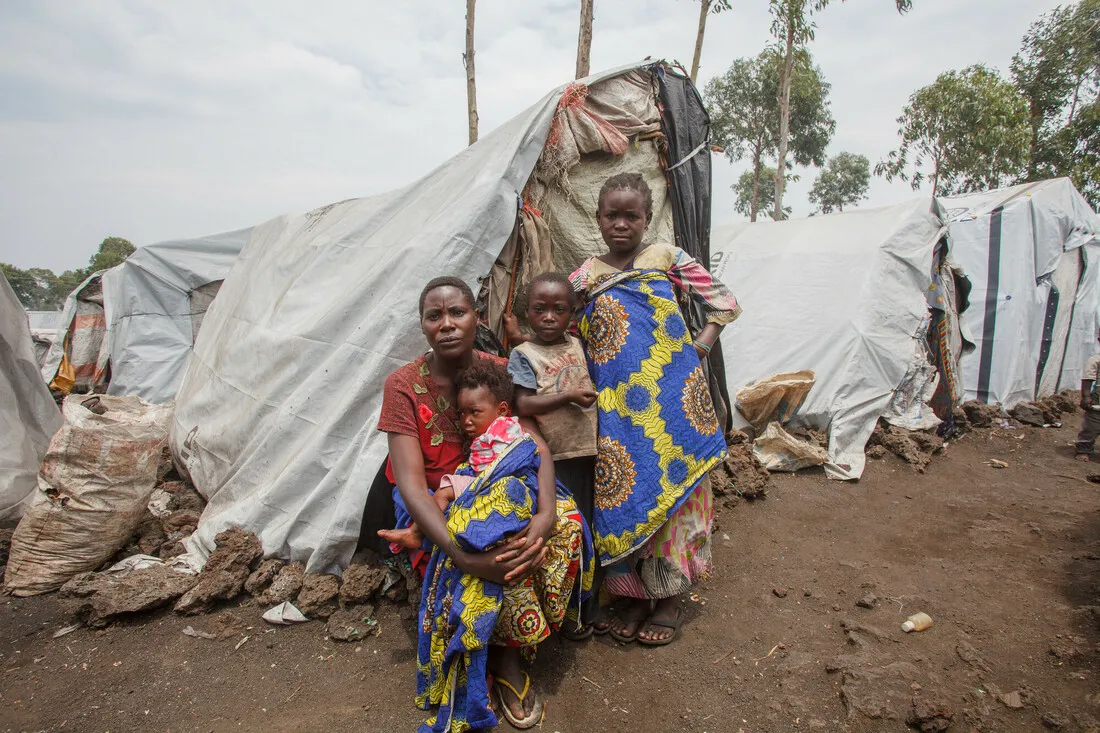 A woman with child in her lap and two children standing next to her.