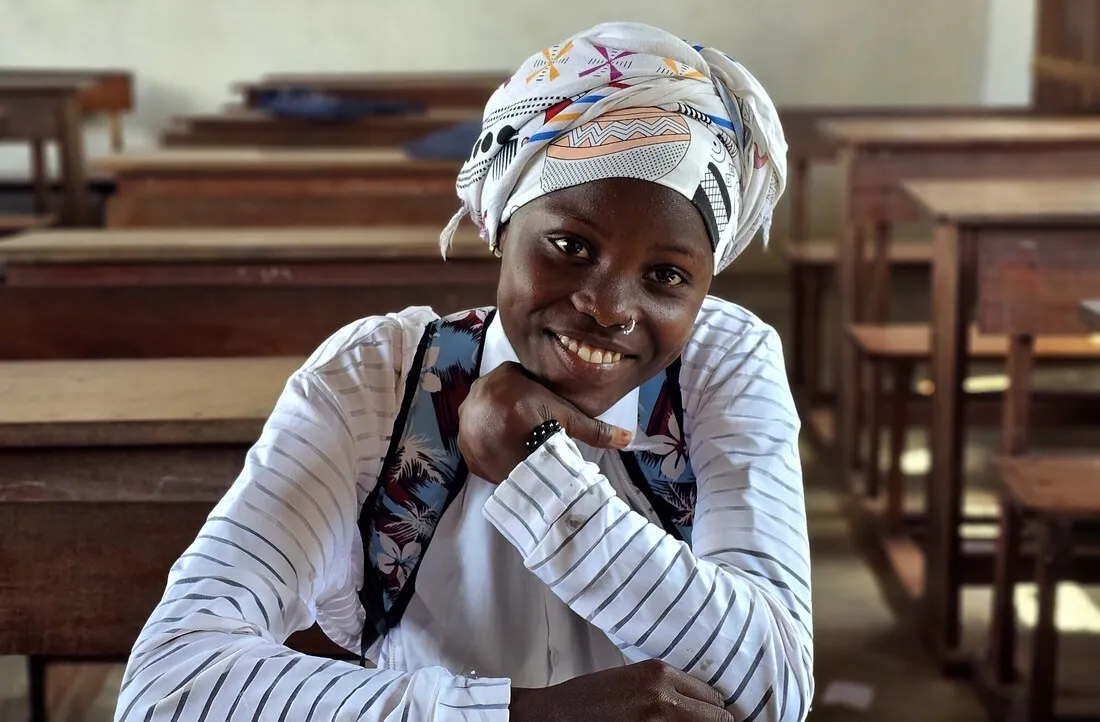 A girl sitting down smiling in a classroom.