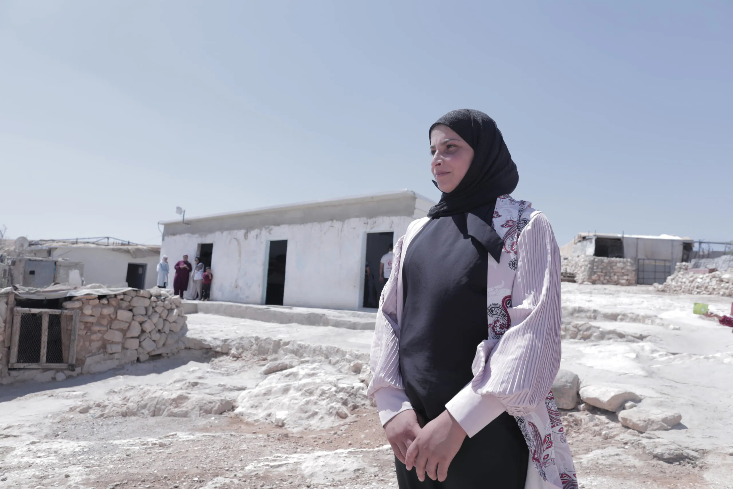 A young woman in a black headscarf looks out over rubble
