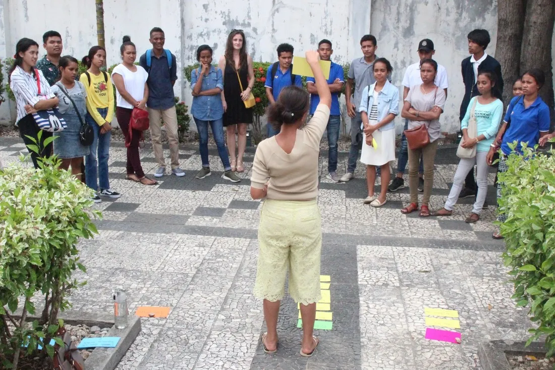 A woman stands in front of a large group of youth. She is holding up cards while they listen.