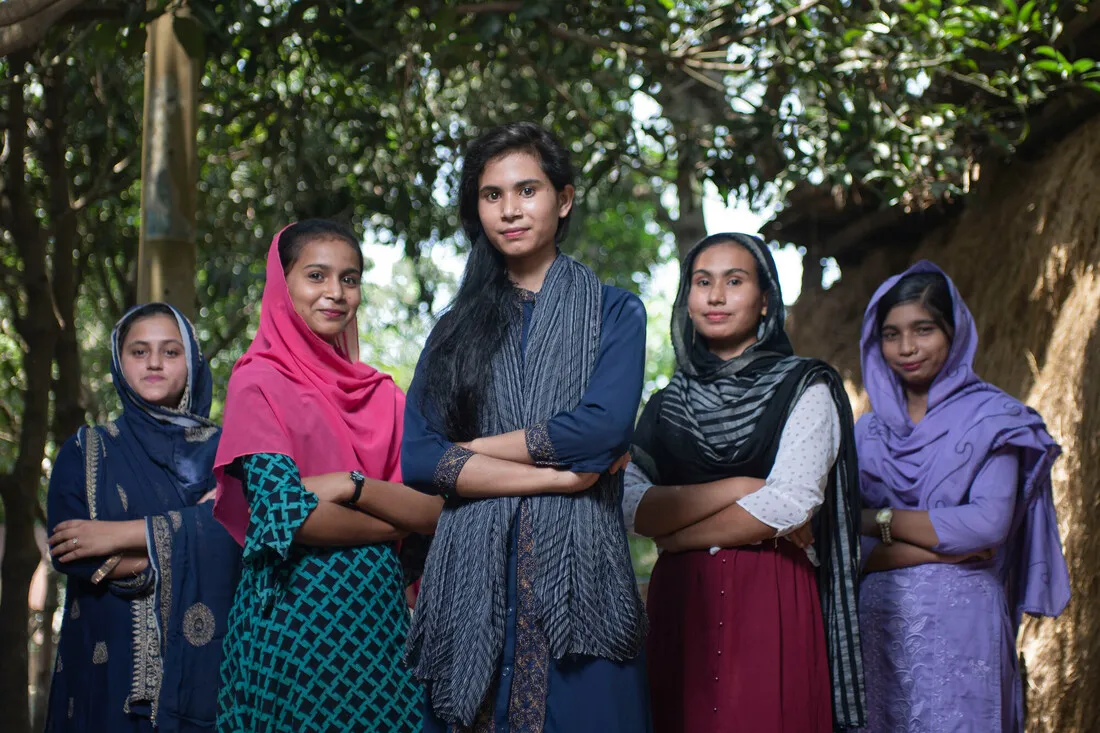 Five adolescent girls standing and smiling with crossed arms.