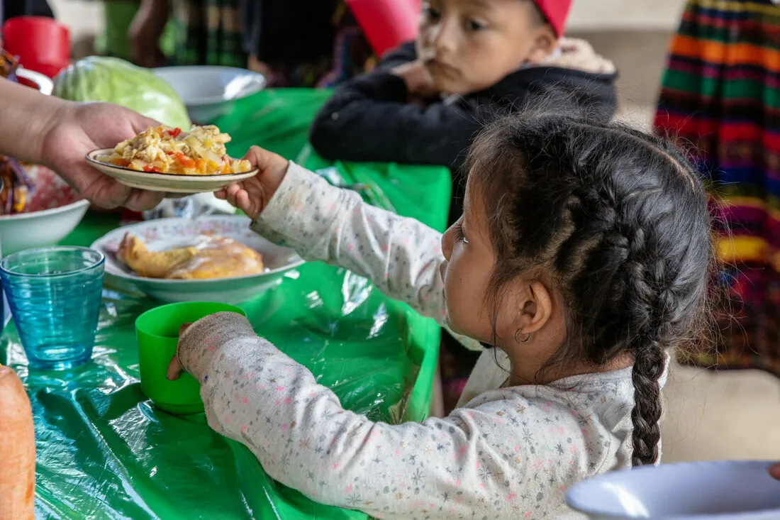 A young girl being handed a plate with food.