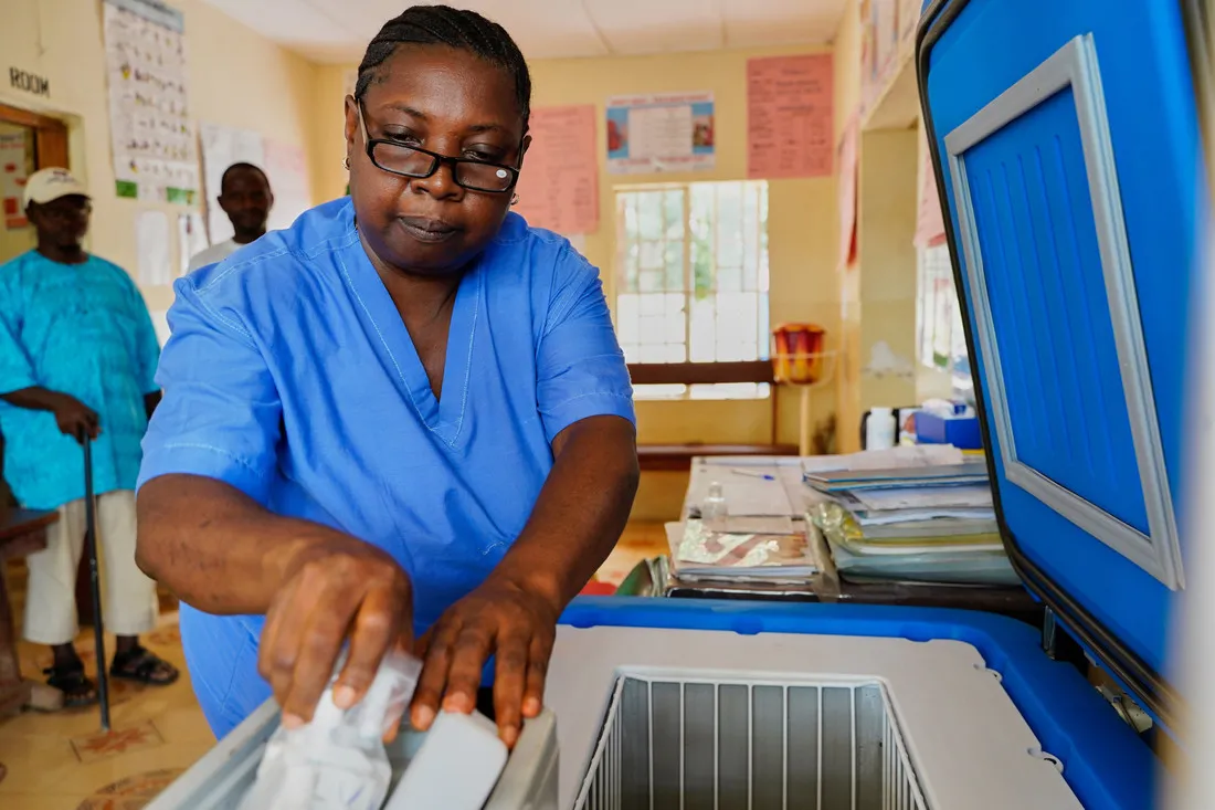 A Black woman wearing blue medical scrubs handles a COVID-19 vaccine.